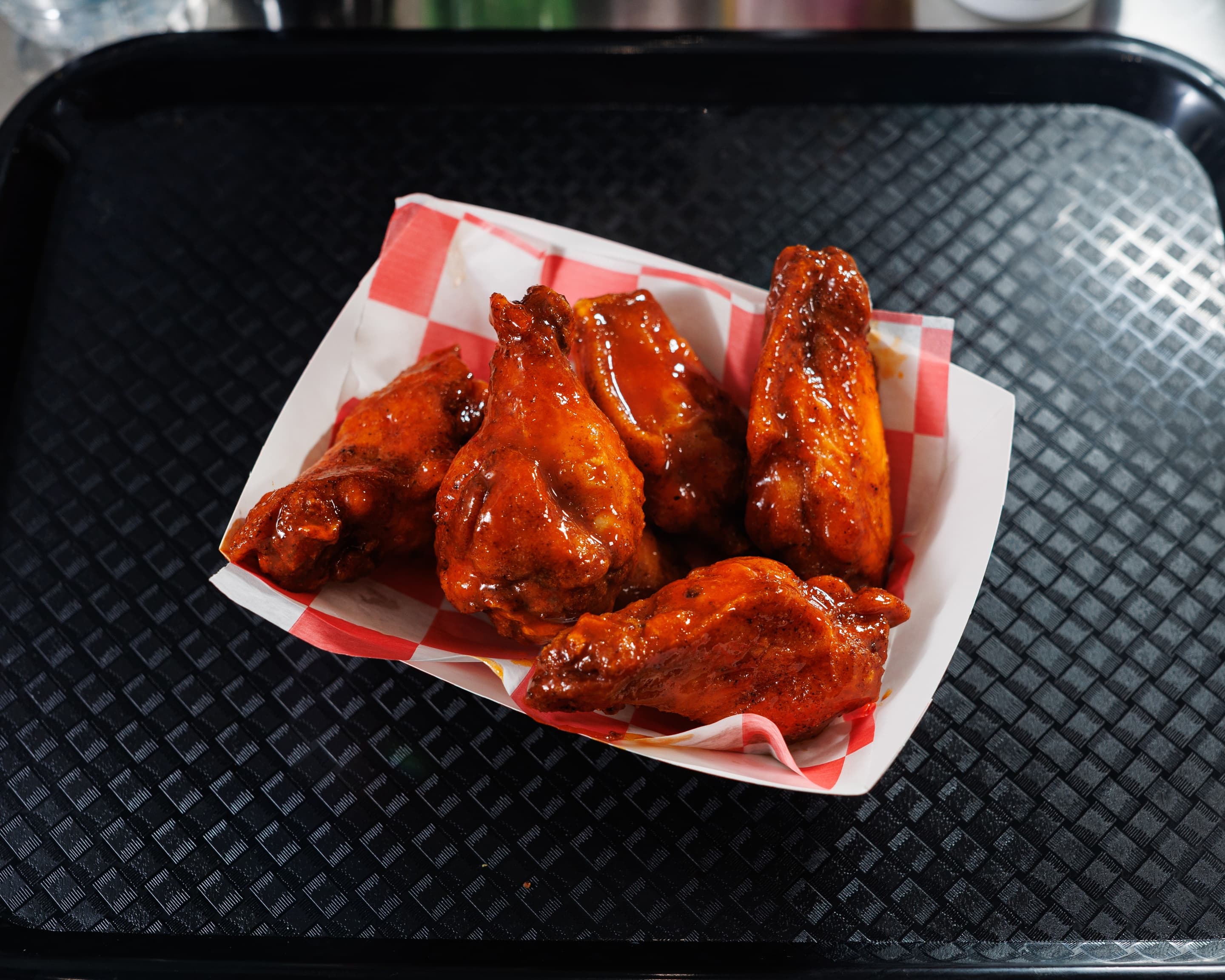 Glossy buffalo sauce wings served in a basket with red checkered paper